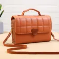Détail de sac bandoulière matelassé marron avec texture fine, double fermeture et fermoir cœur. - Café