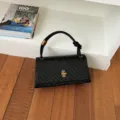 Black woven shoulder bag with gold turn-lock closure and chic knot handle for women commuting. - Black