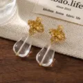 Primo piano dettagliato di lussuosi orecchini floreali dorati con cristalli a goccia trasparenti. - Stile Cristallo Fiore