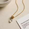 Detailed shot of gold chain necklace with textured knot pendant and clear crystal drop. - Knotted Clear Quartz Necklaces