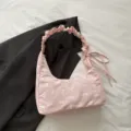Close-up detail of a pink gingham shoulder bag with white bow embroidery and pleated handle. - Pink