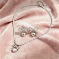 Primo piano dettagliato di collana e orecchini con cuore e fiocco argentato su sfondo rosa. - Set di 3 pezzi / Argento