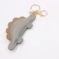 Close-up detail of the cute dinosaur leather keychain with gold hardware and pearl pendant. - Gray
