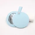 Detailed view of the portable light blue leather makeup mirror with strap and snap button. - Blue
