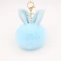 Close-up of light blue fluffy rabbit ear pom pom keychain with gold metal hardware detail. - Light Blue