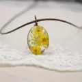 Primer plano de un colgante ovalado de resina y flores secas con collar de cordón marrón. - Amarillo