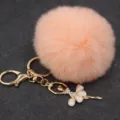 Primer plano de llavero pompón peluche melocotón con dije de bailarina de pedrería brillante. - Bailarina - Pelo de conejo Rex sintético / Rosa