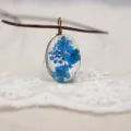 Vista detallada de un collar con colgante ovalado de resina y flores secas azules. - Azul Zafiro