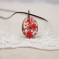 Primer plano detalle colgante ovalado de resina con flores rojas prensadas, delicada joya artesanal. - Rojo