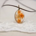 Detalle del hermoso collar con colgante de flor seca de resina ovalada con cordón marrón. - Naranja