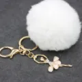 Detalle en primer plano del llavero pompón de felpa blanca esponjosa con colgante bailarina estrás. - Bailarina - Pelo de conejo Rex sintético / Blanco