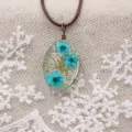 Collar con colgante de flor seca de resina ovalada con flores azules y cordón marrón. - Azul Vintage