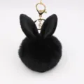 Close-up detail of the black plush bunny ear pom-pom keychain with gold hardware decoration. - Black