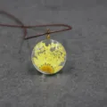 Close-up detail of the clear resin round pendant featuring delicate yellow dried flowers. - 30mm / Yellow