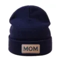 Vue détaillée d'un bonnet en tricot bleu marine avec un écusson en cuir marron et MOM. - Bleu marine