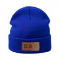 Gedetailleerd aanzicht van blauwe gebreide muts met bruine DAD lederen patch warme muts - Verstelbaar / Saffierblauw