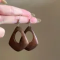 Nahaufnahme Detailansicht von hölzernen geometrischen Ohrringen im Bohostil mit Metallhaken. - Geometrischer Hohlstil (12#) / Braun