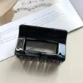 Λεπτομερής κοντινή λήψη της μαύρης γυαλιστερής τετράγωνης τσιμπίδας μαλλιών πάνω σε λευκό χαρτί. - Φωτεινό Μαύρο