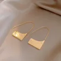 Gros plan détaillé de boucles d'oreilles géométriques en métal doré avec pendentif texturé. - Boucles d'oreilles pendantes rectangulaires en U (57#) / Or