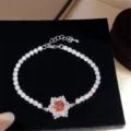 Close-up detail of silver tennis bracelet with orange zircon flower centerpiece and rhinestones. - Red