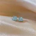Detailed close-up of light blue four-petal flower zircon stud earrings on satin background. - Silver Earring Post - Purple