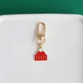 Metal hat pendant keychain detail shot, golden hardware with red enamel decor for bags and keys. - Hat