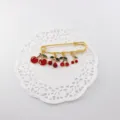 Charming gold-tone safety pin brooch featuring cute red cherry charms with green leaves detail. - Cherry Collection