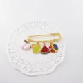 Close-up of a cute gold safety pin brooch featuring colorful enamel fruit charms for summer. - Peach