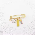 Detail shot of a cute gold-tone safety pin brooch with enamel charms, daisy and blessing tag. - Yellow - Exam Blessing