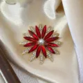 Nahaufnahme einer eleganten, roten Strass-Blumenbrosche mit einer zentralen Perle. - Hellrot