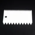 Close-up detail of white plastic serrated cake scraper and dough cutter for baking tool use. - Single Scraper
