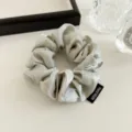 Detailed close-up of an elegant pearl-sheen satin hair scrunchie featuring a handmade label. - Light Green