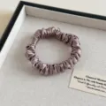 Detailansicht eines mauvefarbenen Satin-Haargummis mit glänzendem Stoff und feiner Struktur. - Grauviolett