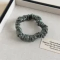 Nahaufnahme eines dunkelgrünen Satin-Haargummis mit glattem Stoff und gerafftem Design Detail. - Bohnengrün