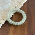 Close-up view of a transparent light green telephone cord hair tie on a wooden tabletop. - Green