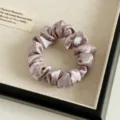 Nahaufnahme eines weichen Satin-Haargummis in Rosa, der glatte und glänzende Stoffstruktur zeigt. - Lotusrosa