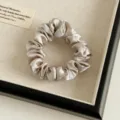 Detailansicht eines eleganten Champagner-Satin-Haargummis, weiches, plissiertes Design für Damen. - Aprikose