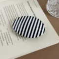 Nahaufnahme der schwarz-weißen gestreiften ovalen Haarklammer auf Buch, elegantes Detail. - Rundclip / Schwarz-weiße Streifen