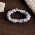 Nahaufnahme des eleganten reinen Seidenhaargummis mit glatter Textur und feinen Falten. - S / Graublau