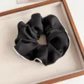 Detailaufnahme eines schwarzen Organza Haargummis mit elegantem weißem Kontrastsaum. - Schwarz