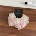 Detailaufnahme des rosa und weißen Organza Haargummis mit Markenetikett auf Holzstruktur. - Rosa Serie