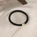 Black braided hair tie with a gold metallic tube detail, elegant and durable design. - Black