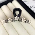 Closeup of a black hair claw clip decorated with white flowers and sparkling rhinestones. - 6.5 Hanger Style / Black