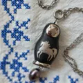 Vue détaillée de collier poupée russe vintage avec pendentif cheval argenté sur tissu. - Colliers matriochka cheval noir argentés