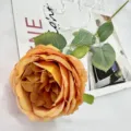 Detailed close-up shot of an artificial orange Austin rose flower with green leaves for home decor. - Orange