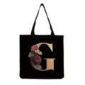 Black canvas tote bag featuring a large gold letter G and vintage floral print details. - Letter G Print (hm3256)
