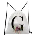 Close-up detail of white drawstring backpack featuring black letter G and watercolor floral print. - Letter G Style