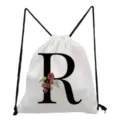 White canvas drawstring backpack featuring a bold black letter R print with delicate floral details. - Letter R