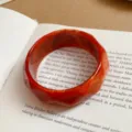 Detailed close-up of a stylish orange geometric faceted acrylic bangle bracelet on a book. - Orange
