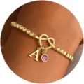 Bracciale di perle dorate con nodo a cuore, lettera iniziale A e pietra natale. - Lettera A / Gennaio (Color Granato)